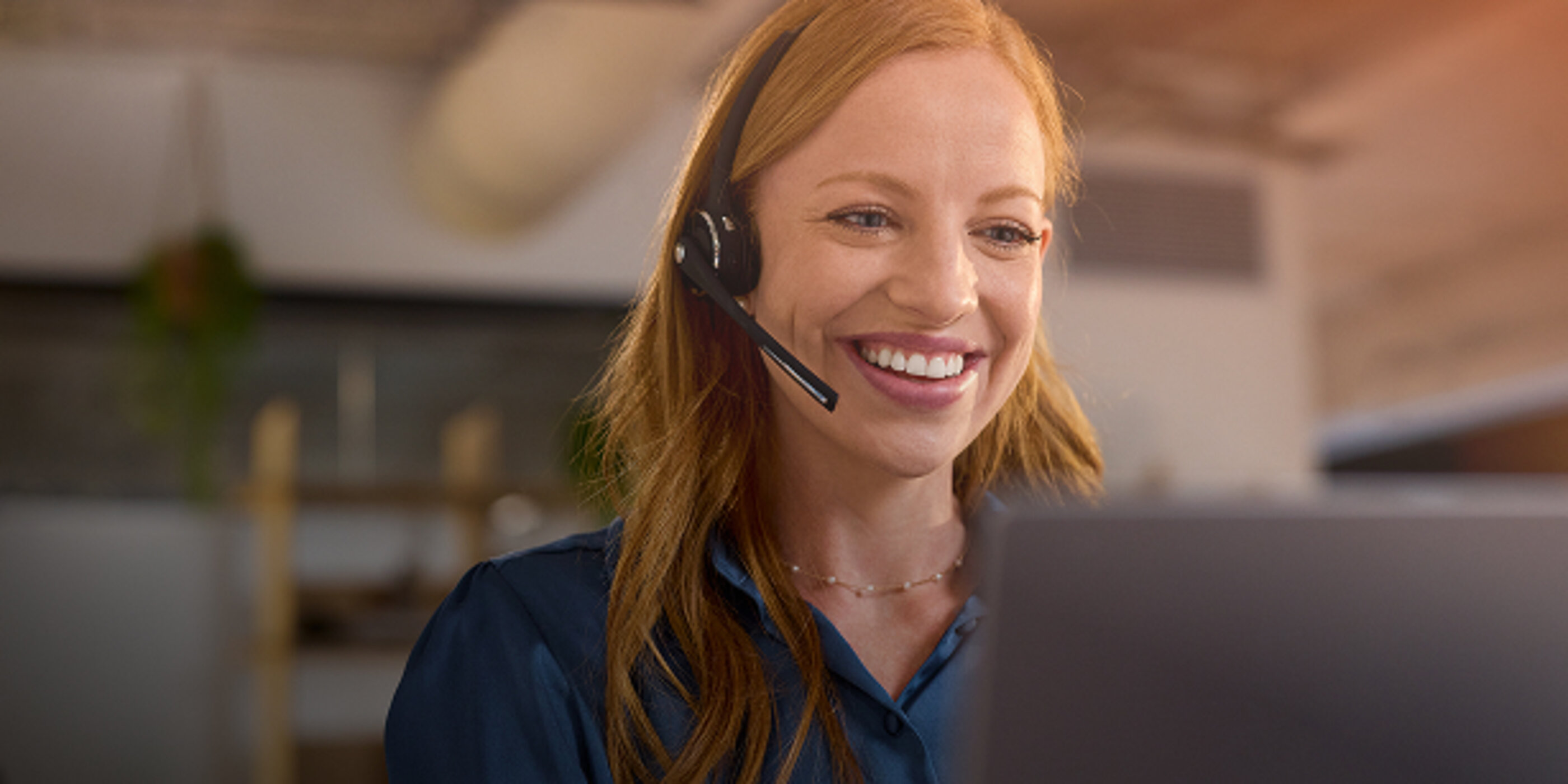 Lächelnde Frau mit Headset vor einem Computerbildschirm im Kundenservice