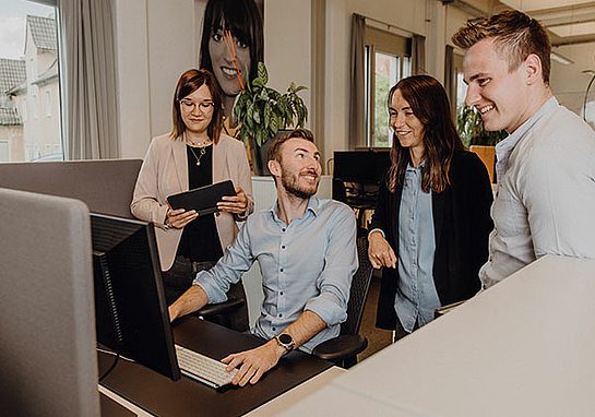 Gruppe von zwei Männern und zwei Frauen steht am Monitor und spricht über die Projektmanagement Jobs bei marcapo