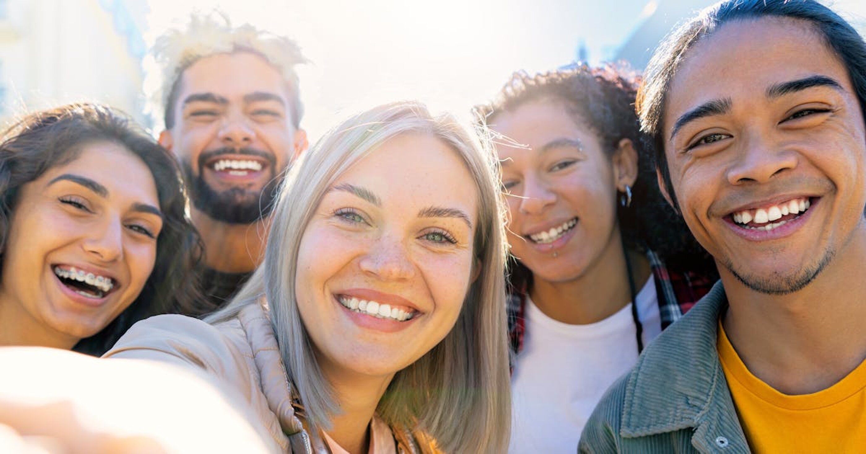 Eine Gruppe diverser junger Menschen schauen lachend in die Kamera