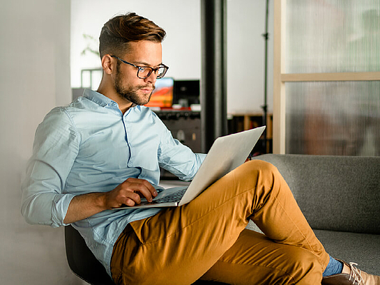 Mann sitzt mit Laptop auf der Couch.
