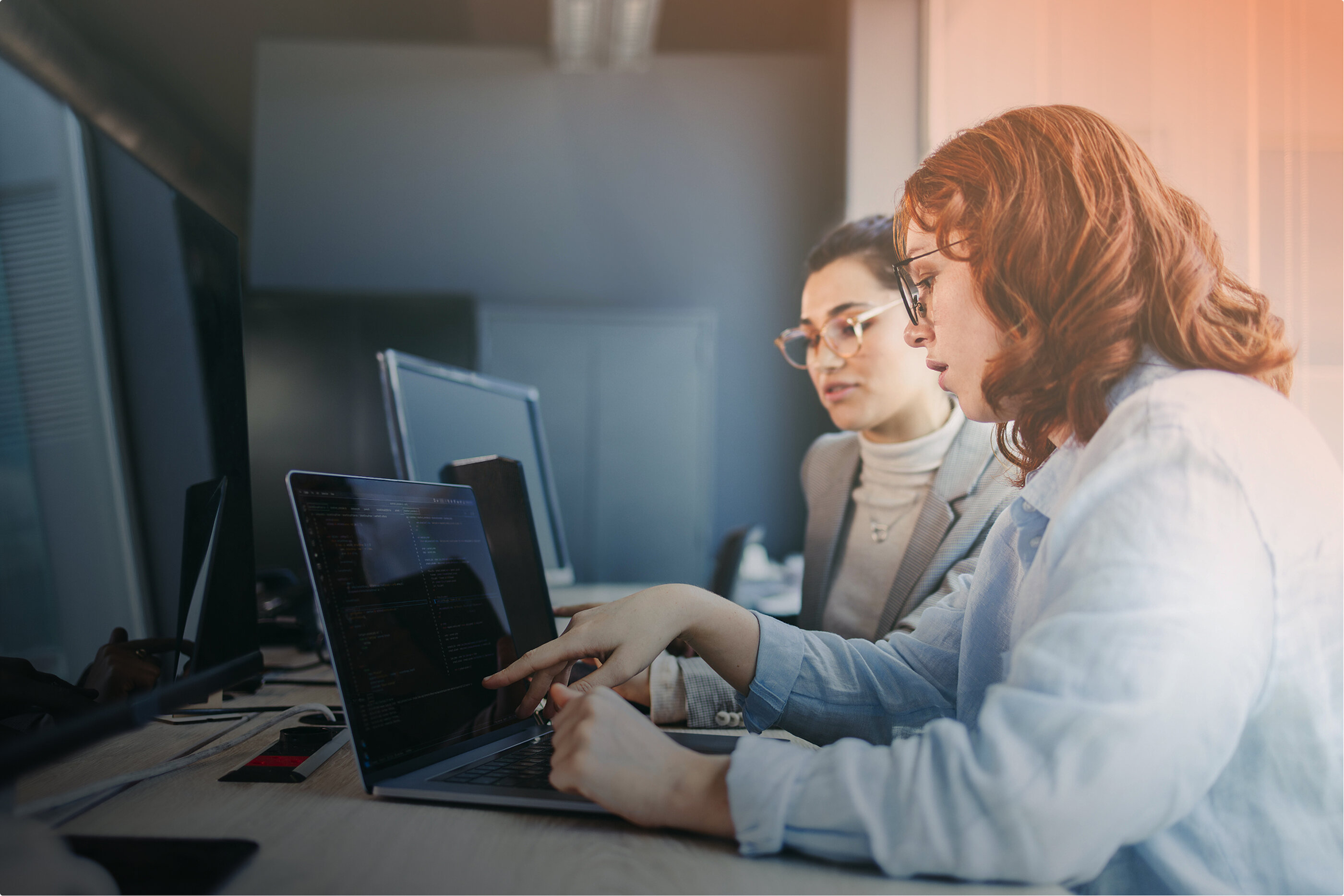 Zwei Frauen sitzen vor ihren Laptops und besprechen etwas miteinander