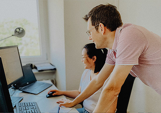 Ein Mann und eine Frau schauen zusammen auf einen Monitor, sie arbeiten in der Technischen Projektleitung bei marcapo