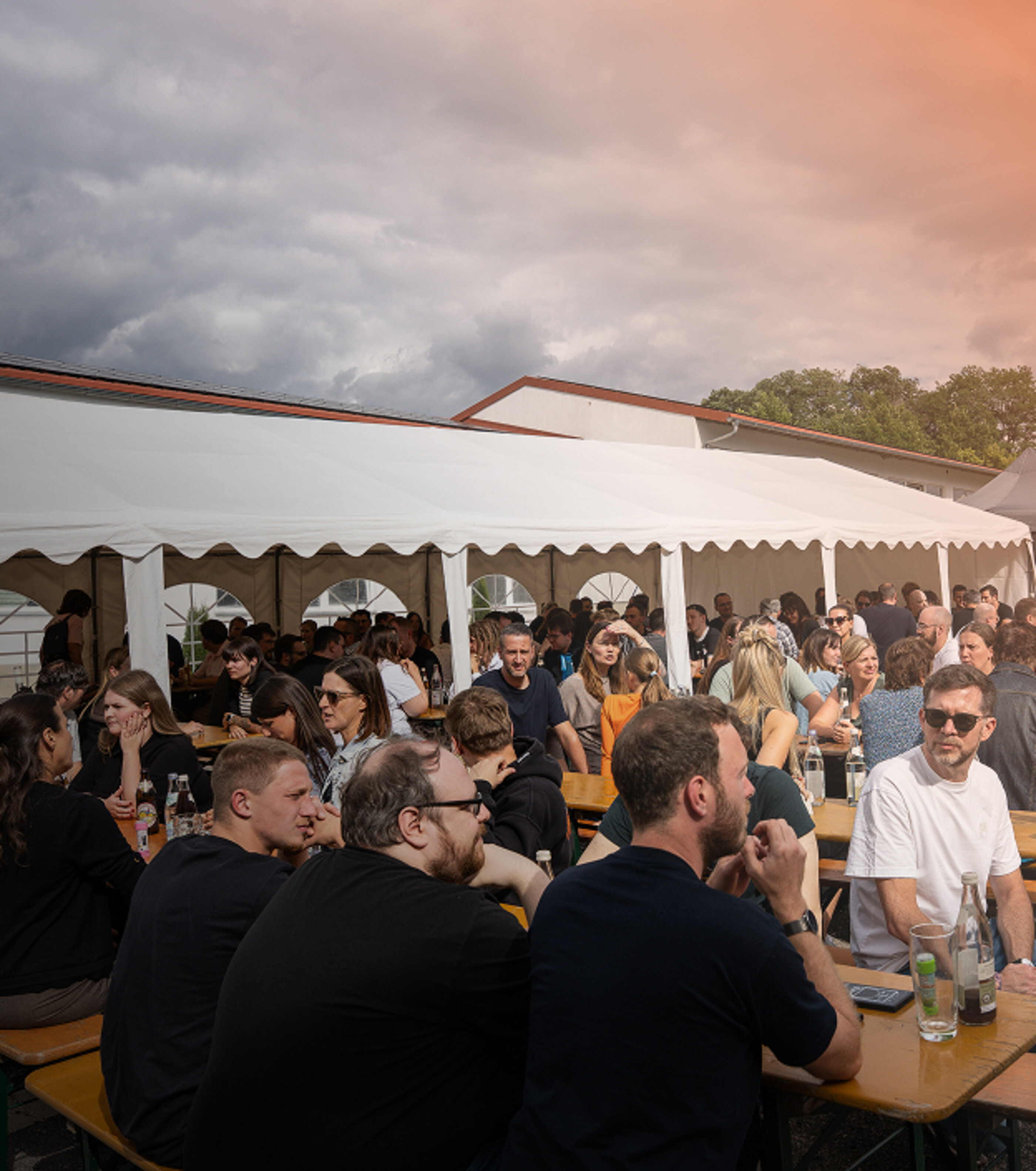 marcapo Mitarbeitende sitzen draußen auf Biergarnituren beim Sommerfest