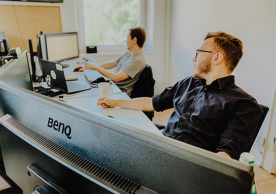 Zwei Männer, die als Product Owner bei marcapo arbeiten, sitzen vor großen Monitoren 