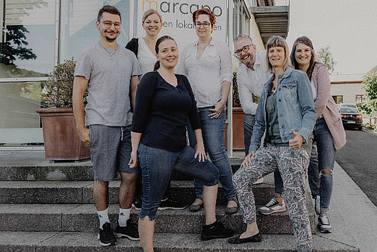 Das Team der Finanzbuchhaltung von marcapo in Ebern steht vor dem Firmenschild