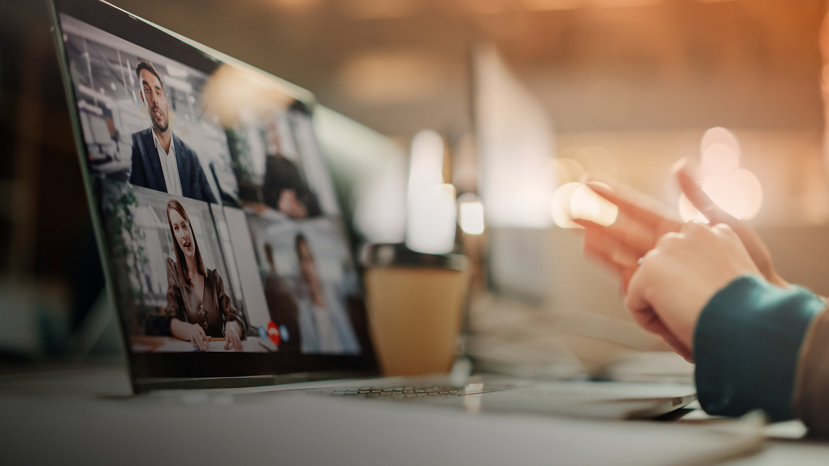 Videokonferenz auf einem Laptop, daneben gestikulierende Hand in heller Büroumgebung