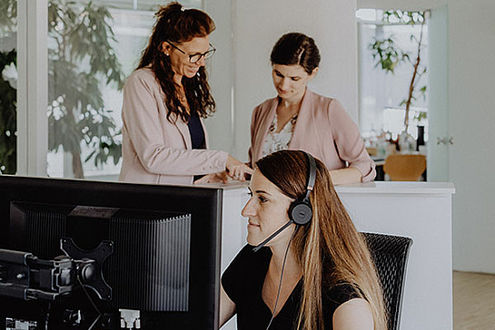 Eine Frau telefoniert, im Hintergrund sprechen zwei Fachkräfte für Bürokommunikation über die neuen Jobs bei marcapo 