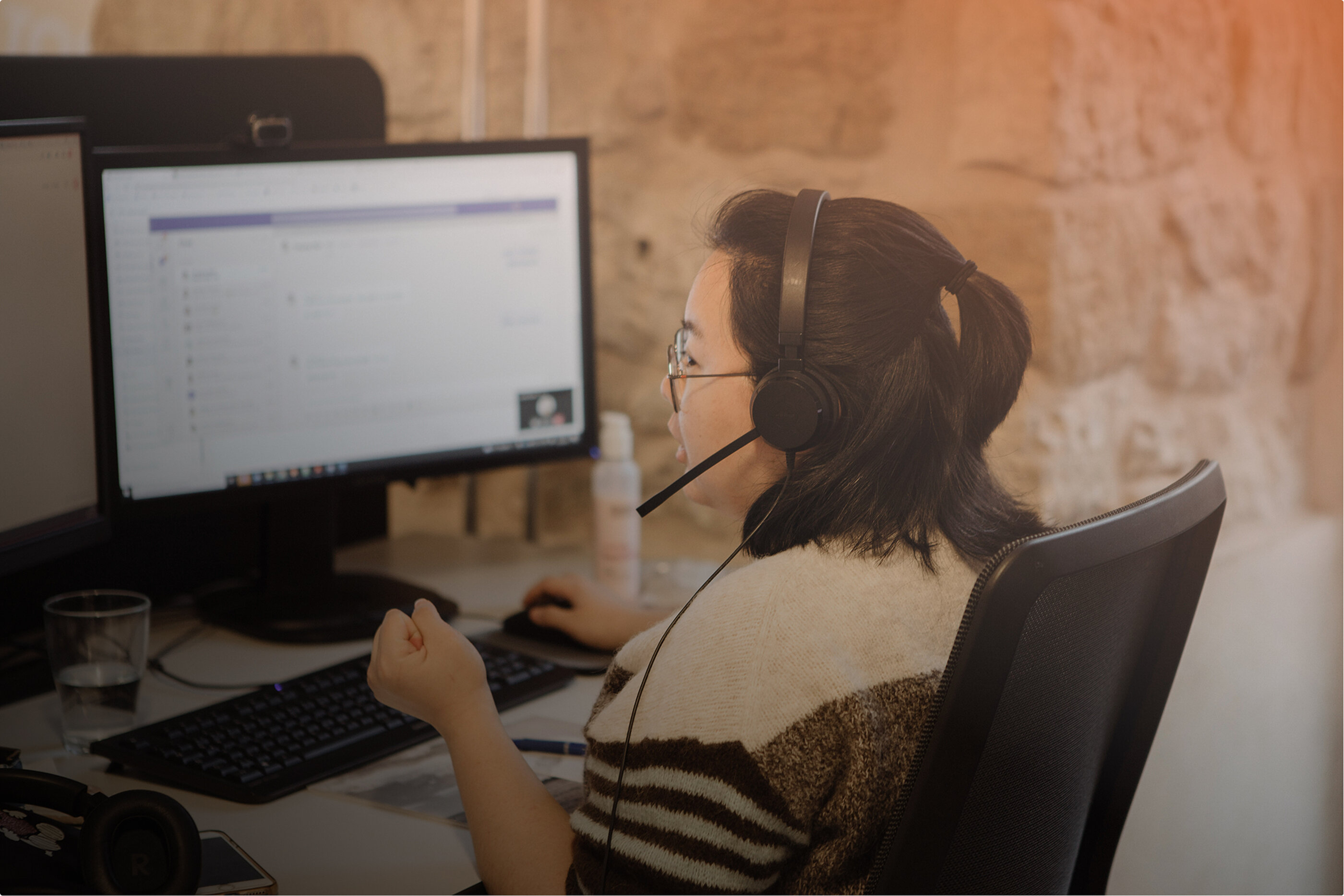 Eine junge Frau mit Headset arbeitet im Büo an einem Computer